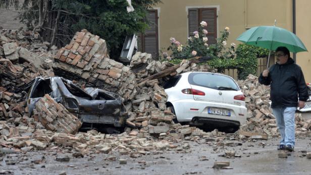 Zwei Autos sind unter den Trümmern eines eingestürzten Gebäudes begraben. Ein Mann mit Schirm geht vorbei.