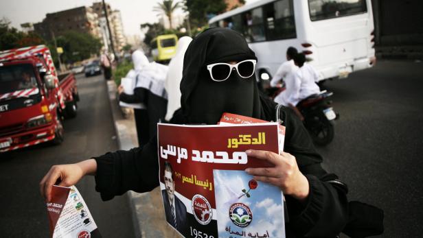 Eine Frau mit Niqab und Sonnenbrille hält ein Wahlplakat von Mohammed Mursi in der Hand.