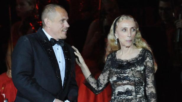 Ein Mann im Smoking legt seine Hand auf die Schulter einer Frau in einem Spitzenkleid.