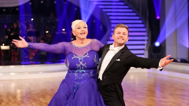 Ein Tanzpaar in festlicher Kleidung posiert auf einer Bühne.