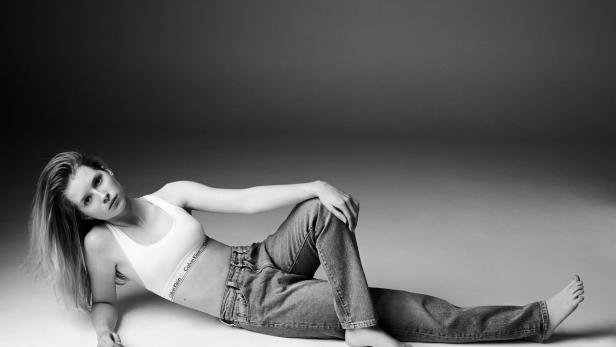 Eine Frau liegt in Jeans und einem Calvin Klein Sport-BH auf dem Boden.