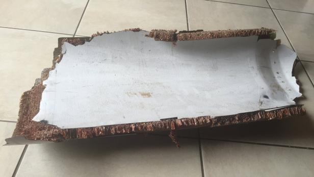 Ein Stück beschädigtes Verbundmaterial mit einer weißen Oberfläche und einer braunen Wabenstruktur liegt auf Fliesen.