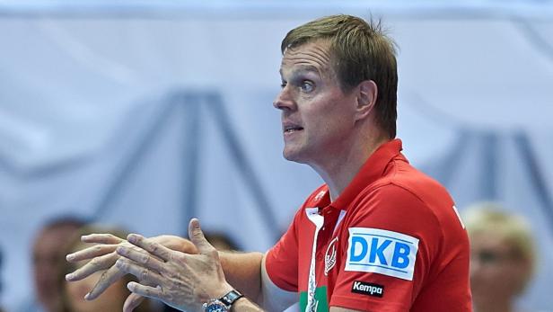 Ein Handballtrainer in rotem Hemd gestikuliert während eines Spiels.