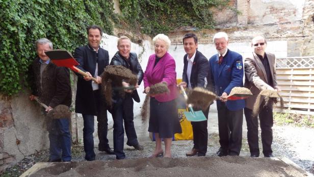 Eine Gruppe von Menschen hält Spaten für einen Spatenstich in die Erde.