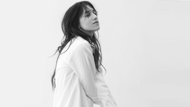 Eine Frau mit dunklen, offenen Haaren und weißem Hemd blickt nach oben.