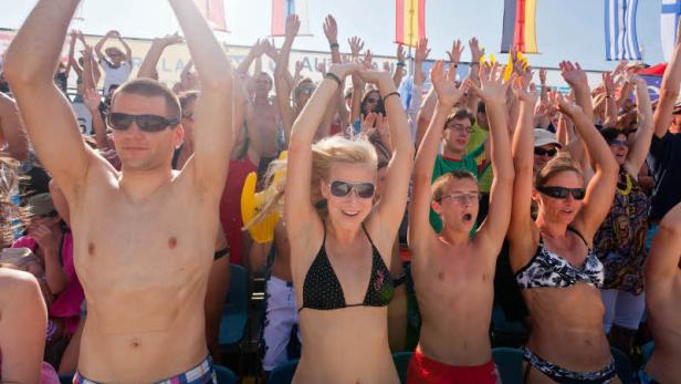 Eine Menschenmenge jubelt mit erhobenen Armen vor einer Reihe von Flaggen.