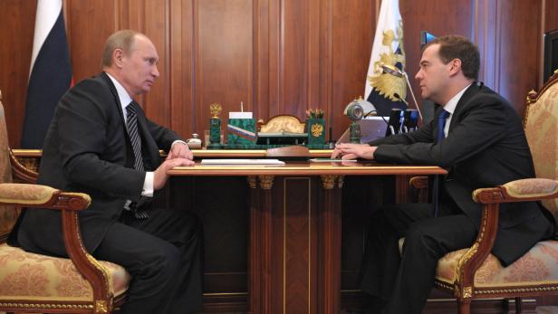 Wladimir Putin und Dmitri Medwedew sitzen sich an einem Tisch gegenüber.