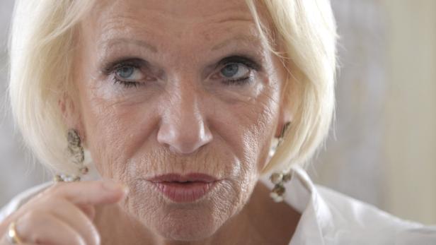 Nahaufnahme einer Frau mit blonden Haaren und Ohrringen, die mit dem Finger zeigt.
