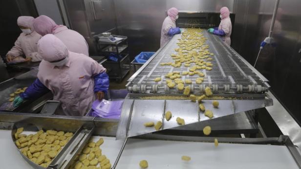 Arbeiter verpacken Chicken Nuggets an einem Fließband in einer Fabrik.