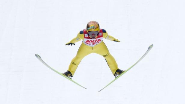 Ein Skispringer in gelbem Anzug während eines Sprungs.