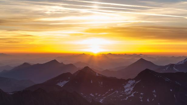 Sonnenaufgang über einer Bergkette mit vereinzelten Schneeflächen.