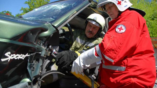 Ein Feuerwehrmann und eine Sanitäterin arbeiten an einem verunglückten Auto.