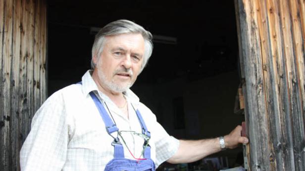 Ein älterer Mann in Latzhose steht in einer offenen Holztür.