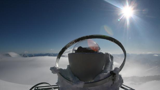 Eine Wetterstation auf einem schneebedeckten Gipfel mit Blick auf eine Wolkendecke.