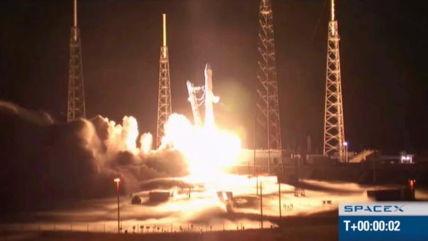 Eine SpaceX-Rakete startet bei Nacht mit hellem Feuer und Rauch.