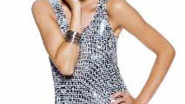 Eine blonde Frau in einem glitzernden Kleid posiert vor einem weißen Hintergrund.
