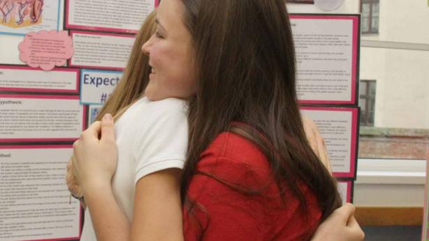 Zwei junge Frauen umarmen sich vor einer Präsentationstafel.