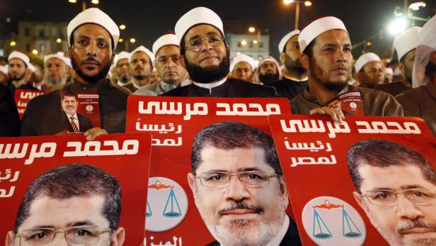 Eine Menschenmenge demonstriert mit Schildern, die das Bild von Mohammed Mursi zeigen.
