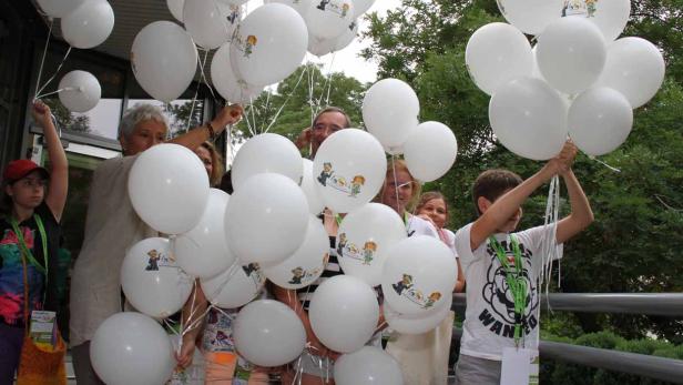 Eine Gruppe von Menschen hält weiße Luftballons mit einer Zeichnung darauf.