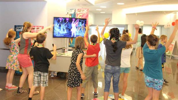 Eine Gruppe Kinder tanzt vor einem Bildschirm, auf dem ein Tanzspiel läuft.