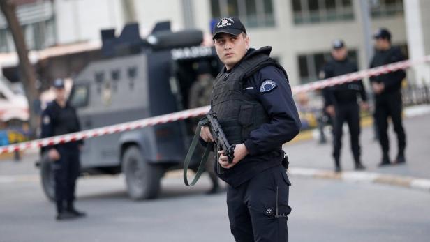 Ein Polizist in Kampfmontur steht mit einem Gewehr vor einem gepanzerten Fahrzeug.