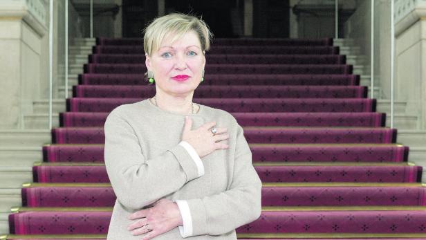 Eine Frau mit blonden Haaren steht vor einer Treppe mit rotem Teppich.