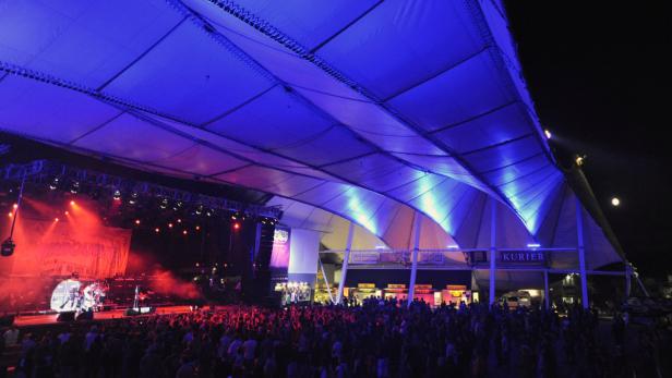 Eine Menschenmenge genießt ein Konzert unter einem großen, blau beleuchteten Zeltdach.
