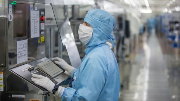 Eine Person in Reinraumkleidung bedient eine Maschine in einer Fabrik.