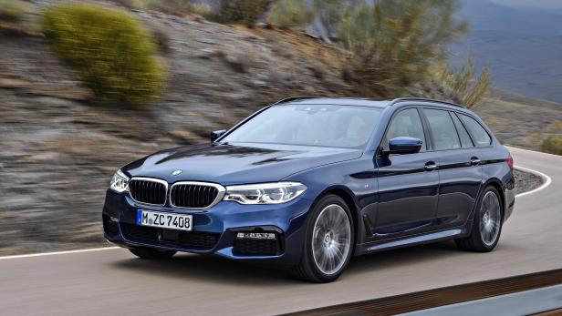 Ein blauer BMW 5er Touring fährt auf einer kurvigen Straße.