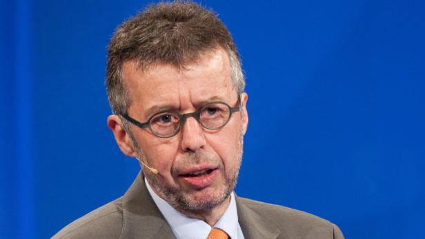 Ein Mann mit Brille und Anzug spricht vor einem blauen Hintergrund.