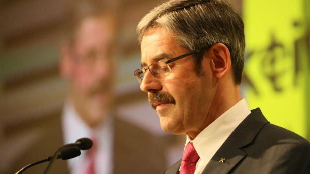 Ein Mann mit Brille und Schnurrbart spricht an einem Mikrofon.