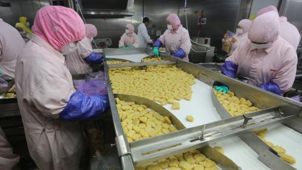 Arbeiter in Schutzkleidung verarbeiten Chicken Nuggets an einem Fließband.