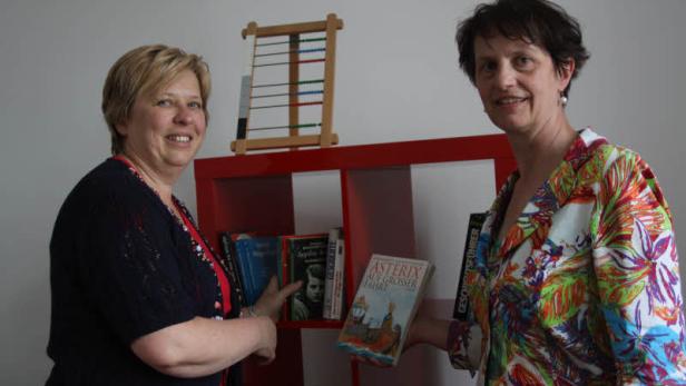 Zwei Frauen stehen vor einem Bücherregal, eine hält ein „Asterix“-Buch.