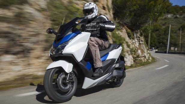Ein Mann fährt einen weißen und blauen Motorroller auf einer kurvenreichen Straße.