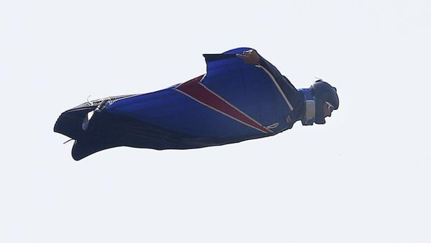 Ein Mann im Wingsuit fliegt vor einem hellen Himmel.
