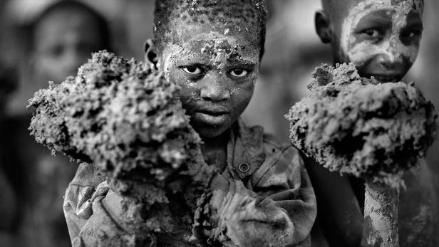 Zwei schmutzbedeckte Kinder halten Klumpen Erde in ihren Händen.