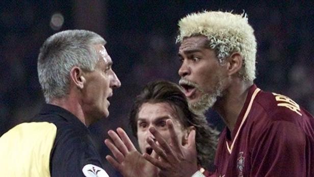 Ein Schiedsrichter diskutiert mit zwei aufgeregten Fußballspielern.