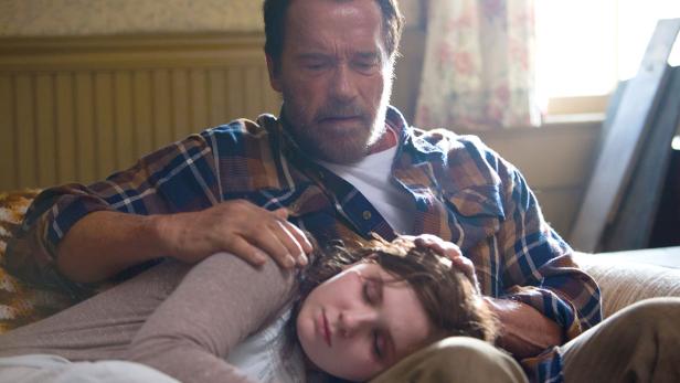 Arnold Schwarzenegger legt tröstend eine Hand auf den Kopf eines schlafenden Mädchens.