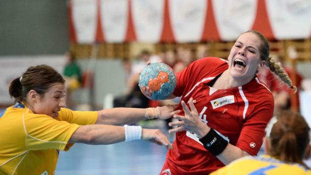 Eine Handballspielerin im roten Trikot wirft den Ball, während eine Gegenspielerin versucht, sie zu blocken.