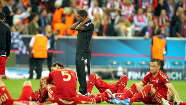 David Alaba steht neben erschöpften Spielern des FC Bayern München auf dem Rasen.