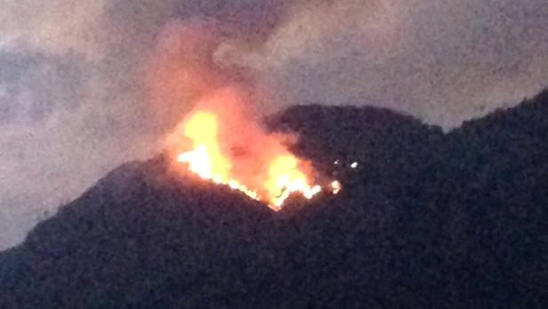 Ein Waldbrand wütet auf einem dunklen Hügel.