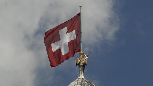 Die Schweizer Flagge weht auf einem Mast vor blauem Himmel.