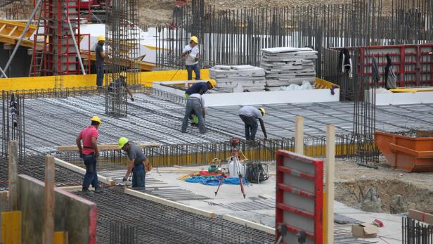 Mehrere Bauarbeiter arbeiten an einem Fundament aus Stahl und Beton.