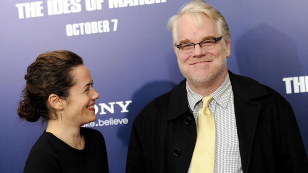 Philip Seymour Hoffman und eine Frau posieren vor einem Poster für den Film „The Ides of March“.