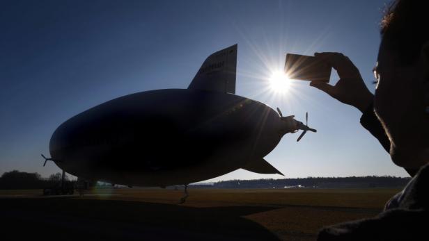Eine Person fotografiert im Gegenlicht einen Zeppelin auf einem Flugfeld.