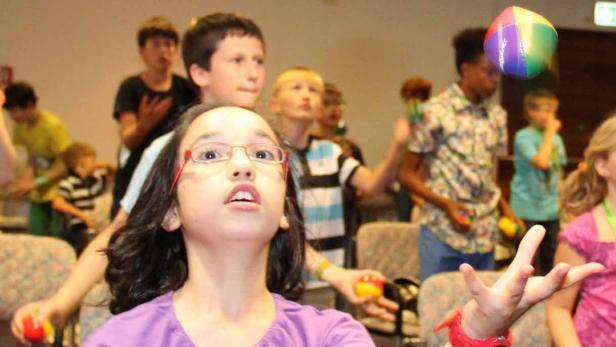 Eine Gruppe Kinder übt sich im Jonglieren mit bunten Bällen.