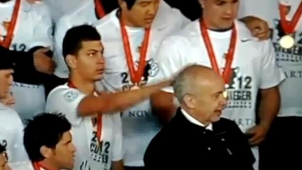 Ein junger Mann berührt den Kopf eines älteren Mannes in Anzug und Krawatte.