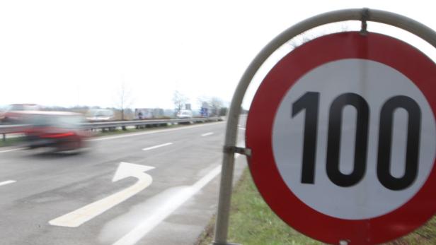 Ein rotes Verkehrsschild zeigt eine Geschwindigkeitsbegrenzung von 100 km/h an einer Autobahn.