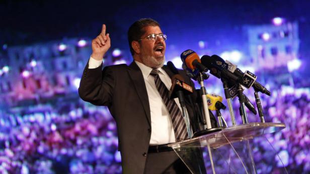 Ein Mann mit Brille gestikuliert an einem Rednerpult vor einer Menschenmenge.