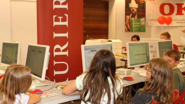 Kinder sitzen an Computern vor einem Banner von Kurier.at.